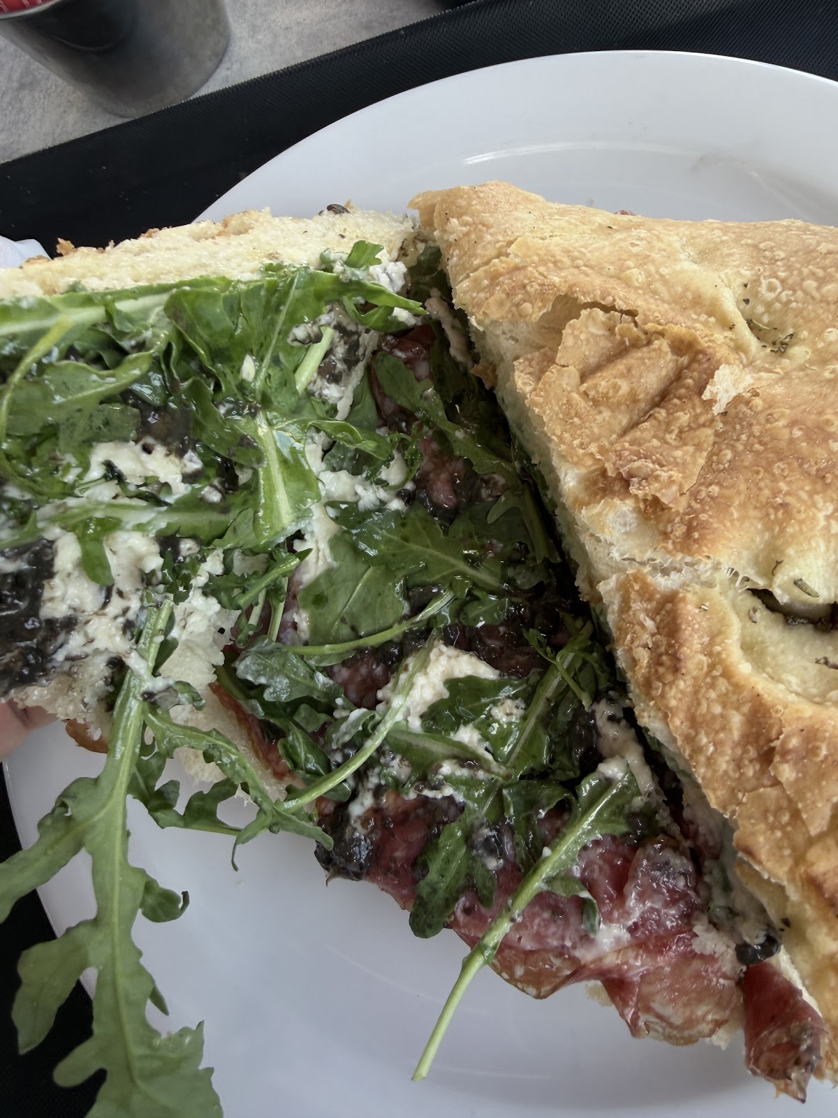 Close-up of a cut focaccia sandwich filled with rocket, salami and crumbled cheese on a dark plate