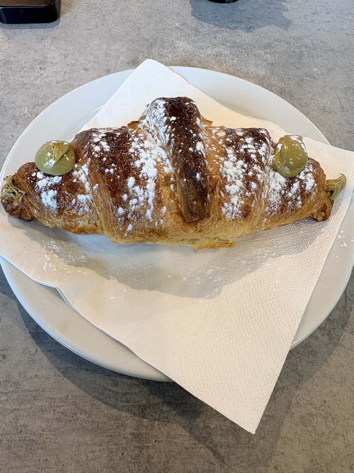 Pistachio-cream croissant dusted with icing sugar on a white plate