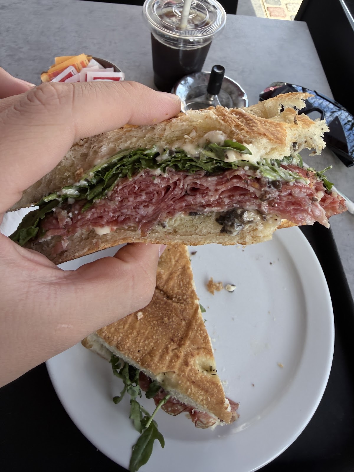 Half a toasted focaccia sandwich with salami and rocket held over the table