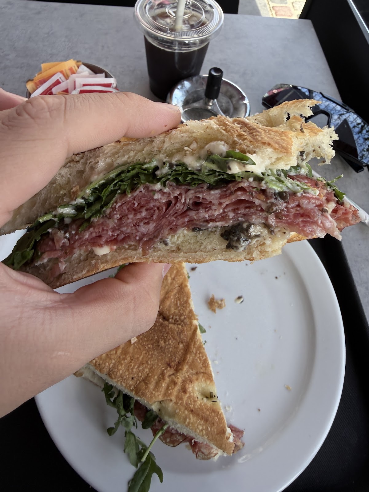 A hand holding half a focaccia sandwich with salami and rocket