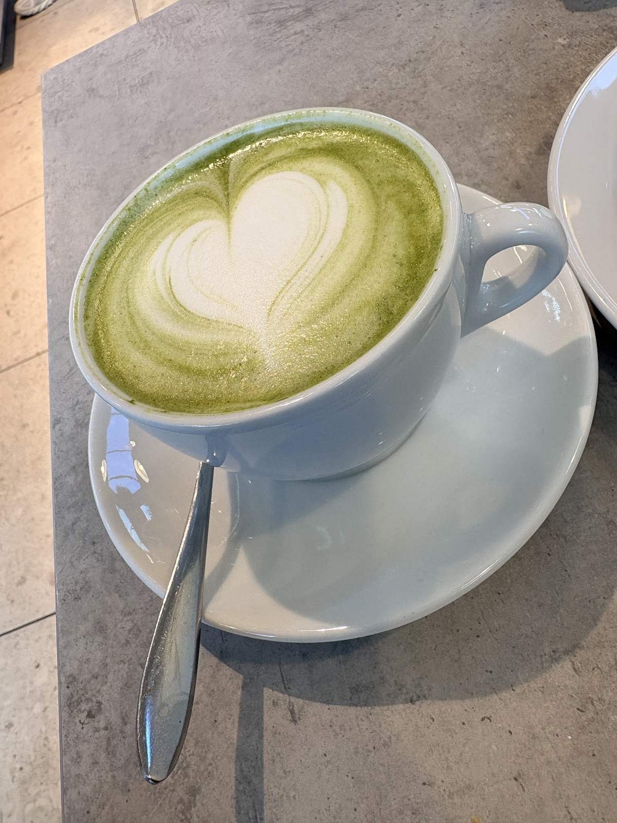 Matcha latte with heart latte art in a cup and saucer on a stone table